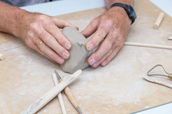 Zwei Hände arbeiten an einem Tonball.