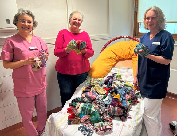 Ulrike Heetlage (m.) von der Initiative Zwergenglück aus Kleve übergibt bunte Mützchen und Söckchen an Dr. med. Ute Janßen, Chefärztin der Klinik für Gynäkologie und Geburtshilfe, und Sabine Toennessen, leitende Hebamme im Kreißsaal des St.-Clemens-Hospitals.