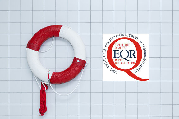 ein rot-weißer Rettungsring hängt an einer hellen gefliesten Wand und daneben ein Foto des IQMG Instituts für exzellente Qualität in der Rehabilitation.