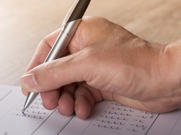 Eine Hand hält einen Kugelschreiber und füllt eine Testung aus.