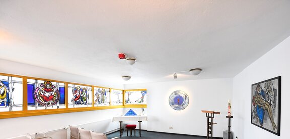 Es ist der helle Innenraum der Kapelle abgebildet. Es gibt bunt bemalte Fenster 