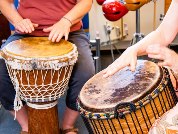 Zwei Rehabilitanden trommeln auf Bechertrommeln.