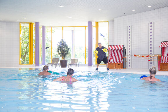 In einem schönen und hellen Schwimmbad bewegen sich drei Rehabilitand*innen im Aqua-Fitness-Angebot. 